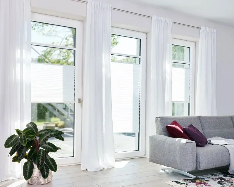 Plissees für das Wohnzimmer oin lichtdurchlässigen Weiß angebracht in Terassentür und bodentiefen Fenstern