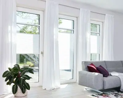 Lichtdurchlässige Plissee in Weiß angebracht in bodentiefen Fenstern in einem Wohnzimmer