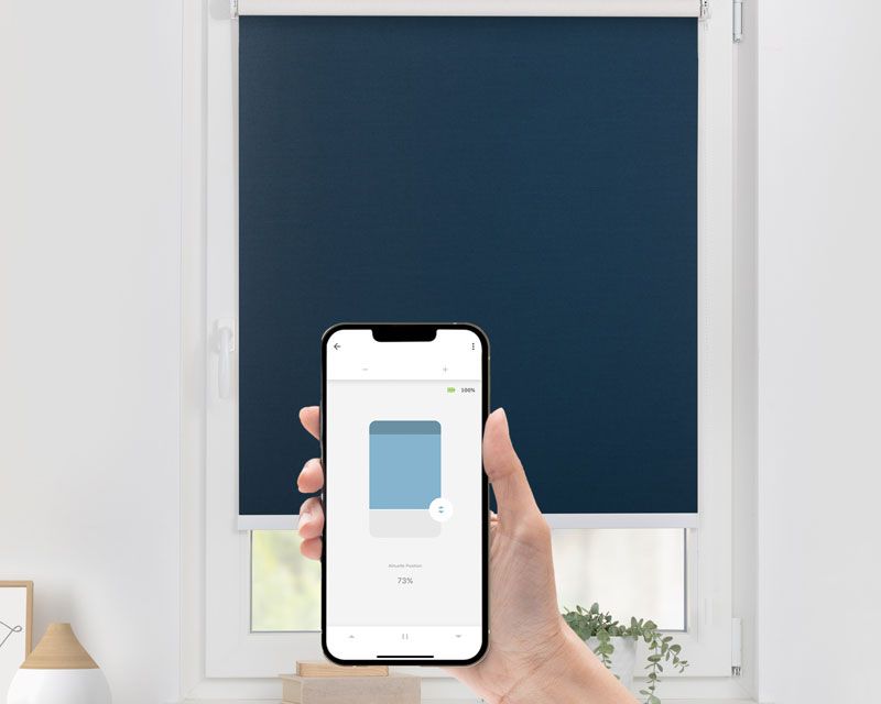 Rollo mit Verdunklungsfunktion und Smart Home Funktion gesteuert per Handy in einem Fenster in blau Rollo mit Verdunklungsfunktion und Smart Home Funktion gesteuert per Handy in einem Fenster in blau