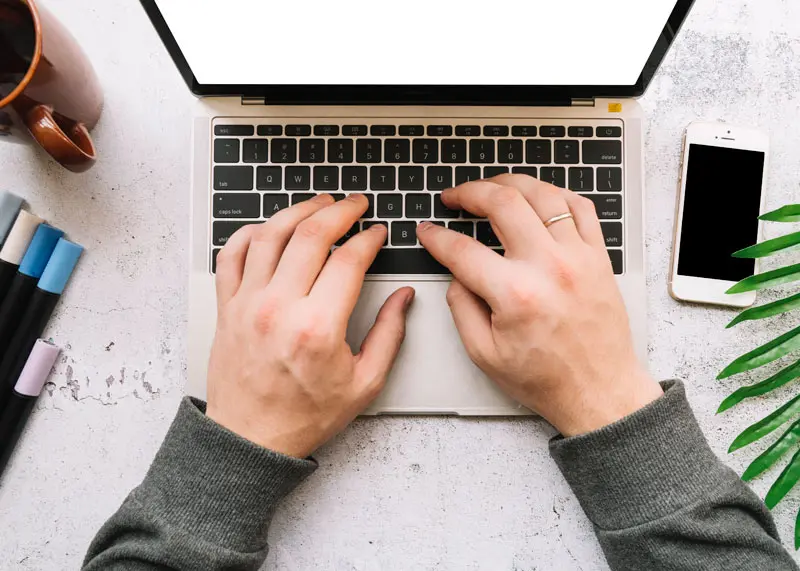 Aufgeklappter Laptop auf einen Tisch mit Handy sowie Stiften und einer Tasse
